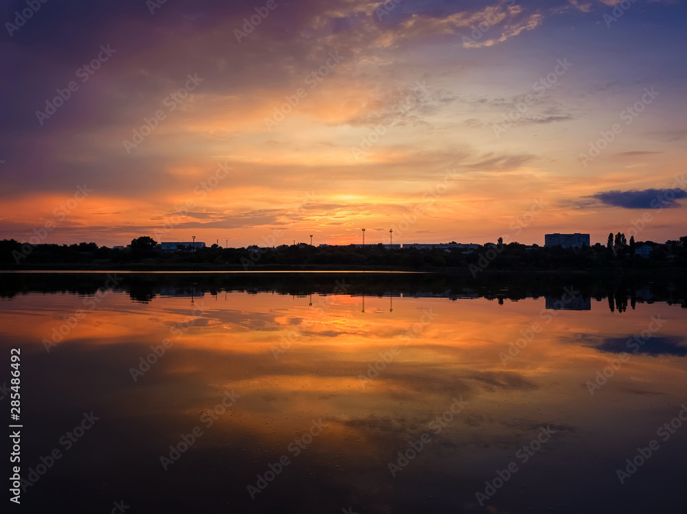 Colorful sunset clouds symmetric reflected on the lake surface. Idyllic summer evening, natural scene near a countryside pond with calm water