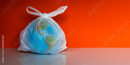 Earth globe in plastic bag on orange background. Environmental pollution and contamination problem concept. Ecology protection, waste reduce and recycle. Save planet, stop plastic idea