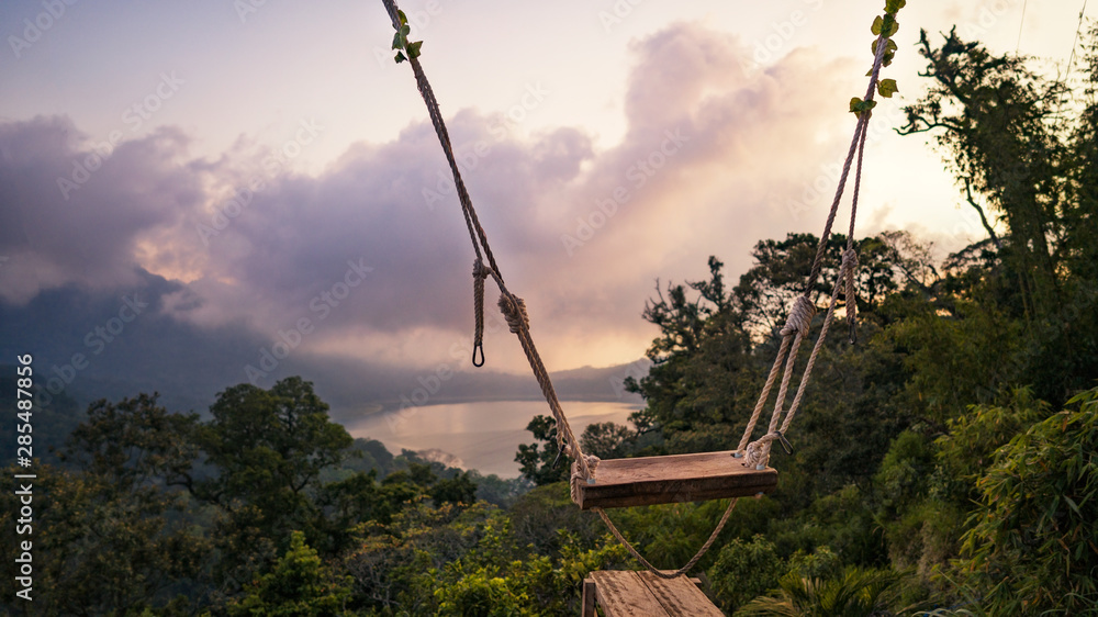 Swing on a cliff at sunset against the lake and forest Swing on a cliff at sunset against the lake and forest