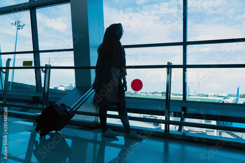 silhouette of hijab Young woman dragging luggage at the airport windowlooking for her flight photo