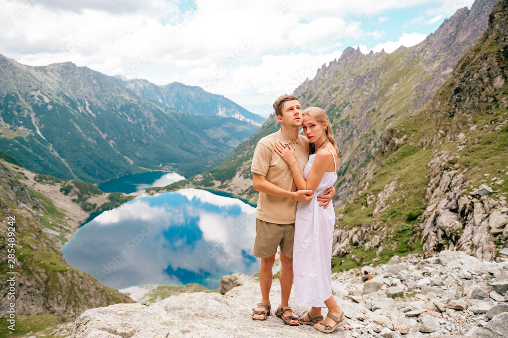 Happy loving couple standing together at stone in High Tatra national park in Poland with a picturesque landscape on background.