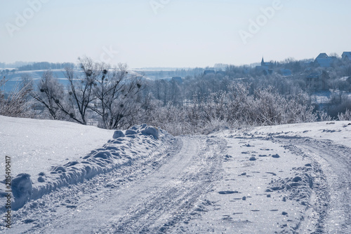 Hard winter snowy glacial rural road and frozen trees with hoarfrost on country landscape background