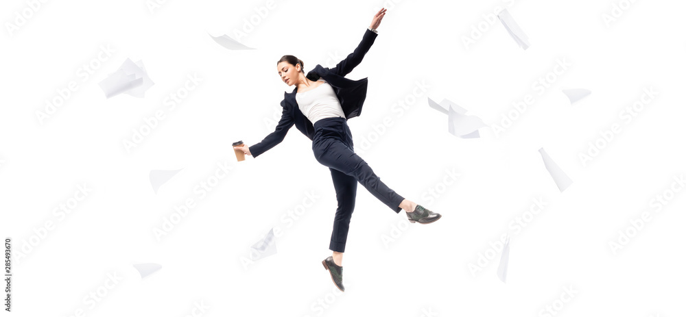 panoramic shot of businesswoman holding paper cup while levitating surrounded with flying papers isolated on white