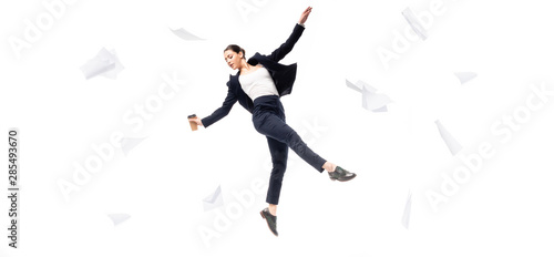 panoramic shot of businesswoman holding paper cup while levitating surrounded with flying papers isolated on white