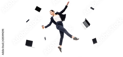 panoramic shot of businesswoman holding paper cup while levitating surrounded with flying laptops and smartphones isolated on white