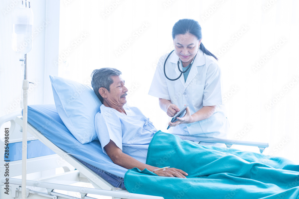 Asian woman professional doctor with notepad smiling, visiting, talking, and diagnosing the old man patient lying in patient’s bed at hospital ward Asian woman professional doctor with notepad smiling, visiting, talking, and diagnosing the old man patient lying in patient’s bed at hospital ward