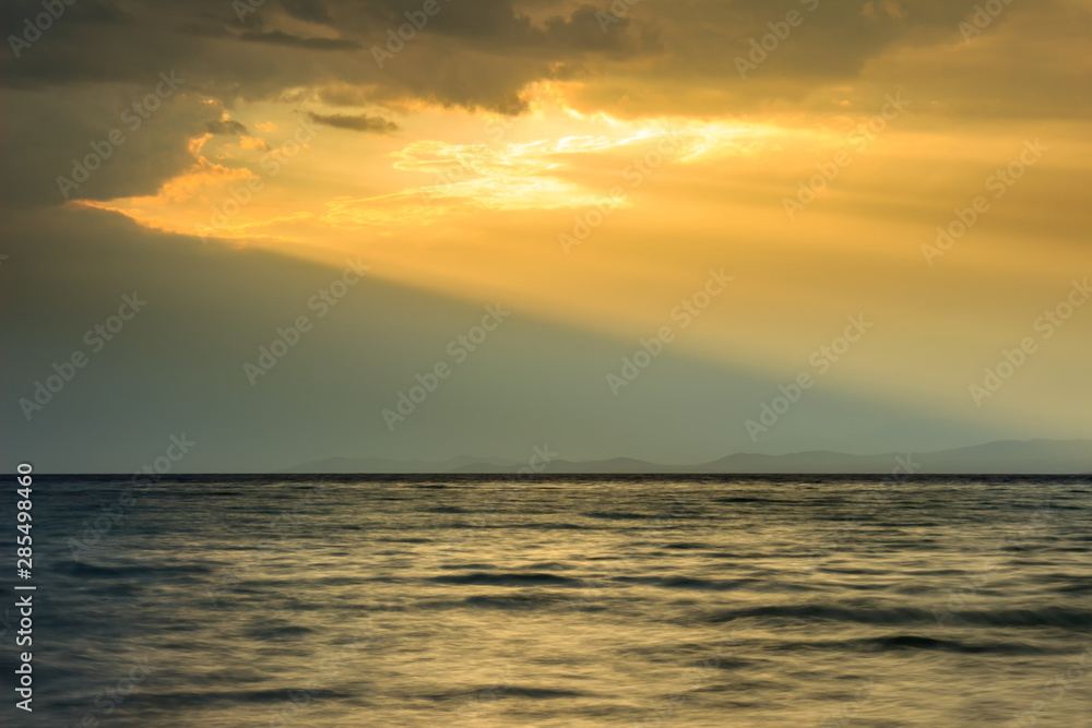 Amazing golden sun-rays passing through the large hole in dramatic clouds over the sea
