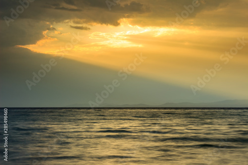 Amazing golden sun-rays passing through the large hole in dramatic clouds over the sea