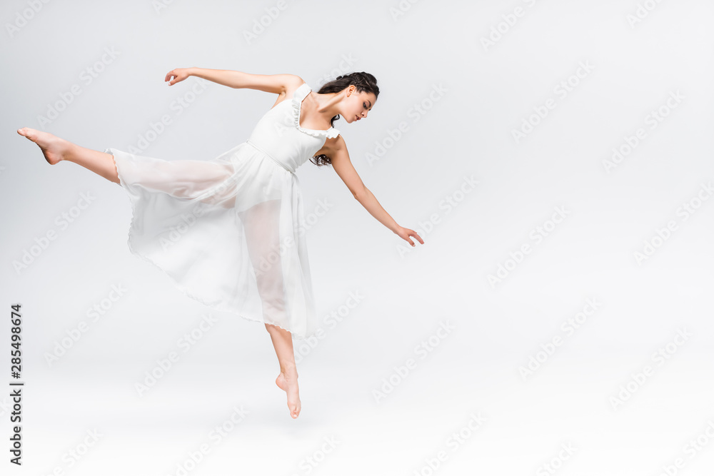 attractive young ballerina dancing in white dress on grey background