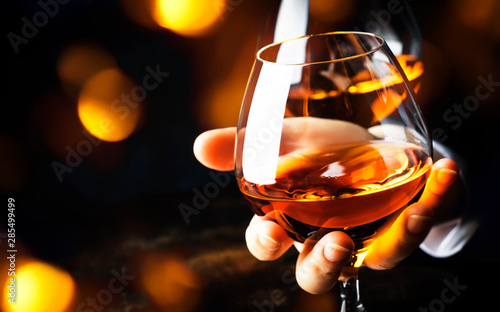 French glowing cognac glass in hand on the dark bar counter background, copy space, selective focus photo