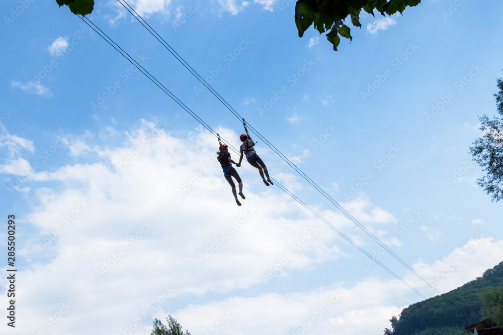 Two girls hold hands and walk along a zip line, a sport in an extreme park.