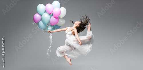panoramic shot of graceful ballerina dancing with festive balloons on grey background