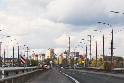 The highway in the industrial zone. Plant with high pipes and road with traffic. Environmental pollution