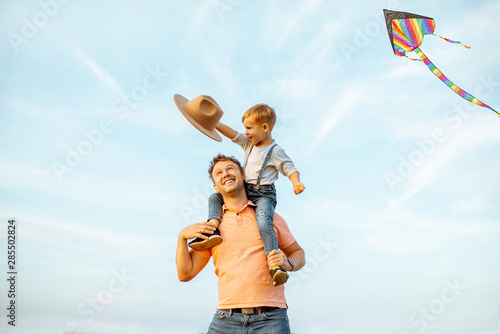 Принти на полотні Portrait of a happy father with young son riding on the shoulders on the blue sky background outdoors