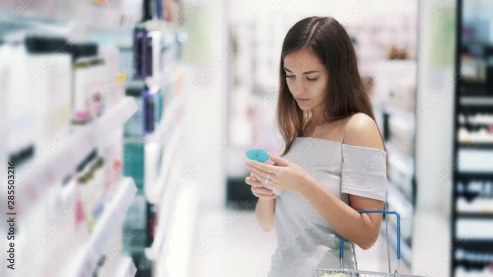 Woman in cosmetics shop chooses shower gel, reads label, sniffss it, slow motion Woman in cosmetics shop chooses shower gel, reads label, sniffss it, slow motion