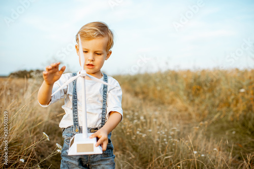Portrait of a curious young boy playing with toy wind turbine in the field, studying how green energy works from a young age