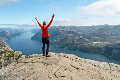 Sportive girl with raised hands standing on the rock near Preikestolen, Norway, Lusefjord sea view.