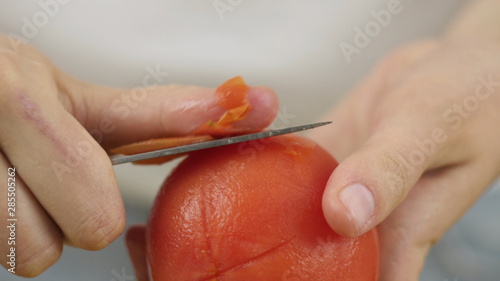 Man or woman peels off a tomato with a knife. Preparation of products for cooking