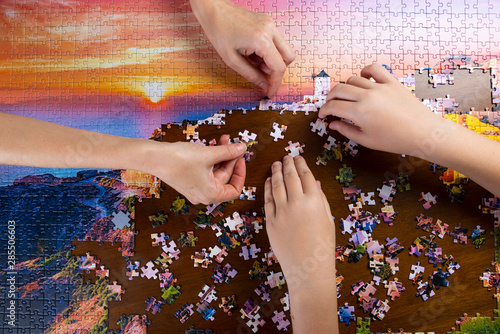 children and adult hands stack color puzzle on wooden table photo