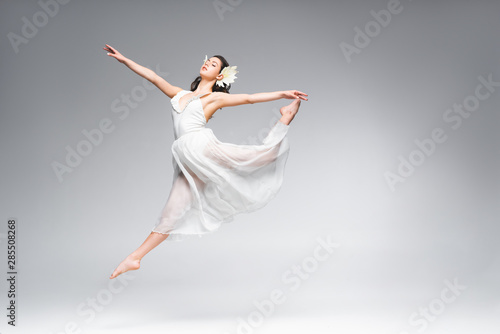 Fototapeta Naklejka Na Ścianę i Meble -  beautiful young ballerina in white dress dancing on grey background