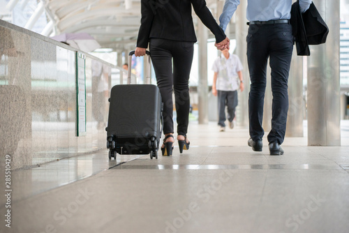 Businessman and Businesswoman Dragging suitcase luggage bag,walking to passenger boarding in Airport.Couple of love travel to work.Asian tourist wearing black suit pull trolley bag. Business Travel co