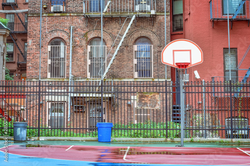 Empty basketball court on a rainy day. Surrounded by a fence and between homes. Harlem, NYC, USA.