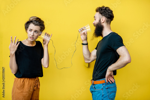 Man and woman talking with string phone made of cups on the yellow background. Concept of communication