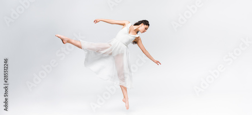 panoramic shot of graceful ballerina dancing on grey background