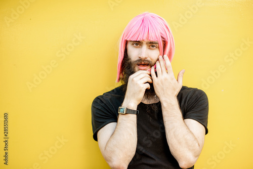 Funny portrait of a stylish playful man with beard and long color hair with expressive emotions on the yellow background photo