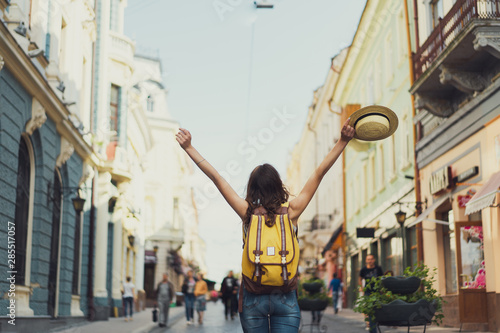 Back view of a young woman traveler with a backpack on her shoulder out sightseeing in a foreign city, stylish female foreigner examines architectural monument during her long-awaited summer vacation