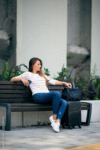 Woman waiting on the bus station and sitting on bench.Next to her luggage.
