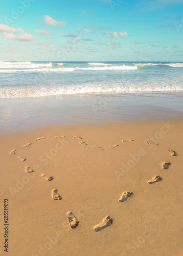 Footprints in the sand, heart shaped. Love traveling imprint on beach