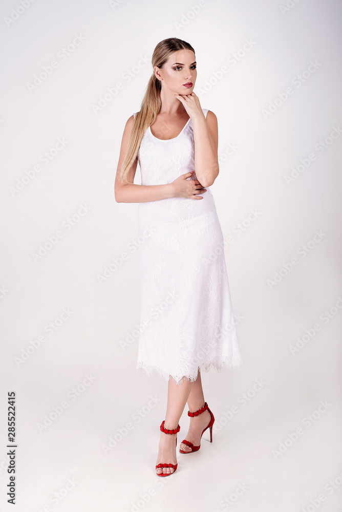 Young attractive sexy blond woman model with light hair, wearing white dress and sandals on heels, posing in white studio Young attractive sexy blond woman model with light hair, wearing white dress and sandals on heels, posing in white studio