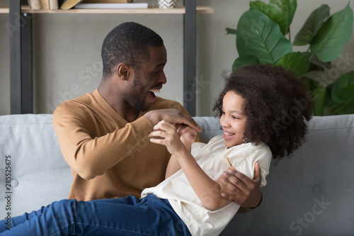Happy African American father playing with preschool daughter at home