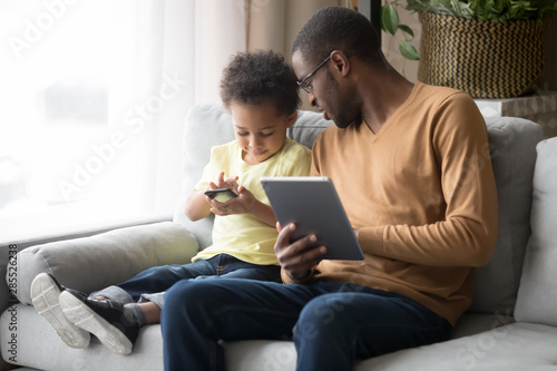 Loving African American father teaching toddler son to use phone