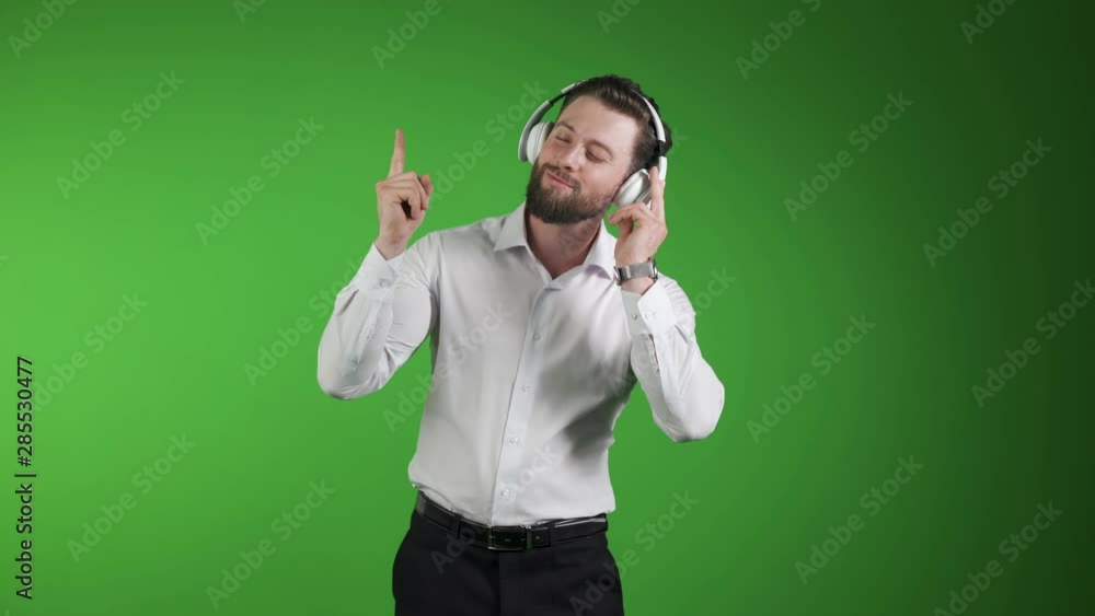 young handsome man on green studio background, isolated, listening to music on earphones, smiling, happy. Dancing to the rythm. young handsome man on green studio background, isolated, listening to music on earphones, smiling, happy. Dancing to the rythm.