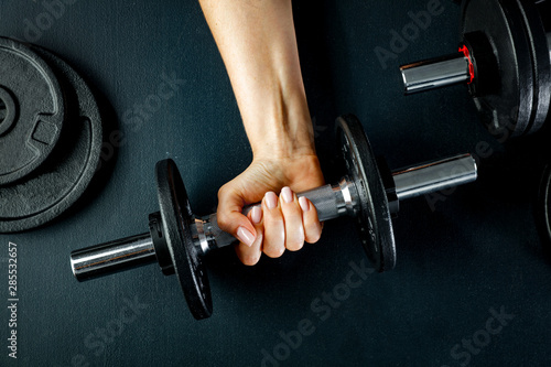 A woman and workout in the gym. Barbell, dumbbell held in hand on black background.