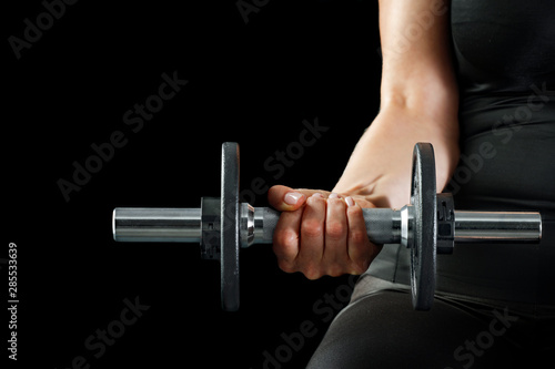 A woman and workout in the gym. Barbell, dumbbell held in hand on black background.