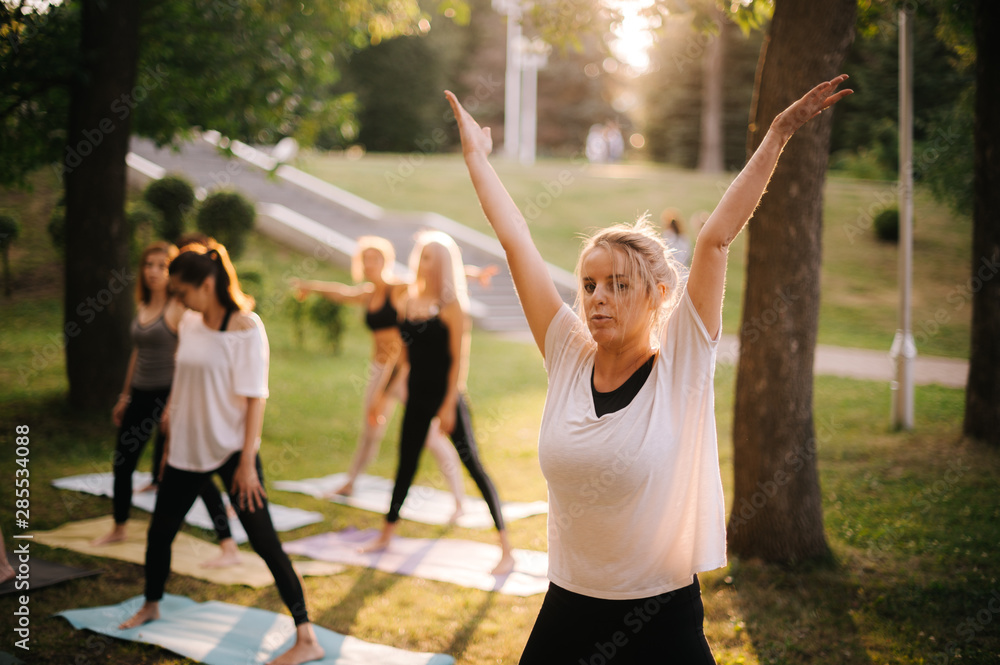 Group of young women do yoga in city park on summer sunny morning under guidance of instructor Group of young women do yoga in city park on summer sunny morning under guidance of instructor