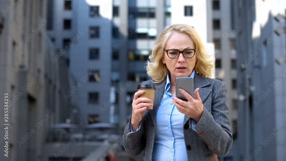 Worried female manager reading smartphone news holding cup of coffee, technology