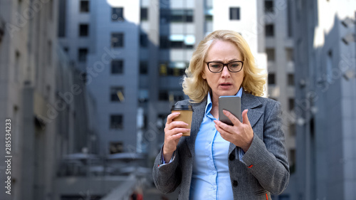 Worried female manager reading smartphone news holding cup of coffee, technology