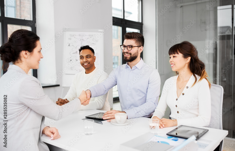 job, hiring and employment concept - international team of recruiters having interview with female employee and shaking hands at office job, hiring and employment concept - international team of recruiters having interview with female employee and shaking hands at office