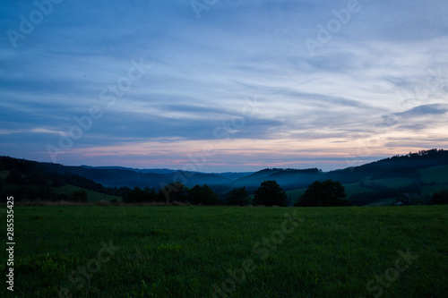 Morning sunrise in Beskyd area colored dark sky with clouds and fresh fog covering grass around mountains and hills behind in the valley.