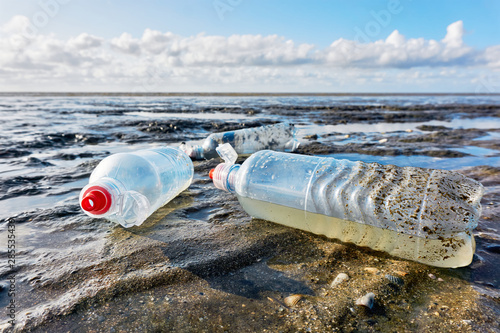 Plastic bottles with red bottle caps on a beach with blue sky at low tide. Concept of plastic pollution of the sea and marine life. Beat Plastic Pollution. 