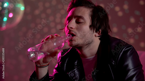 Man drinking vodka from bottle at party, suffering depression, alcohol addiction