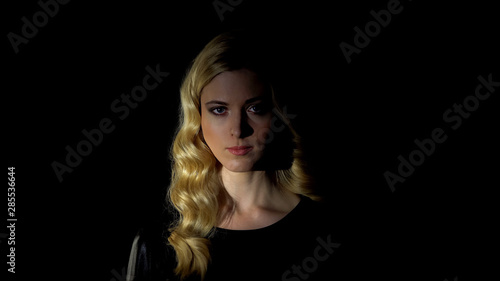 Beautiful woman looking at camera against dark background, femininity concept