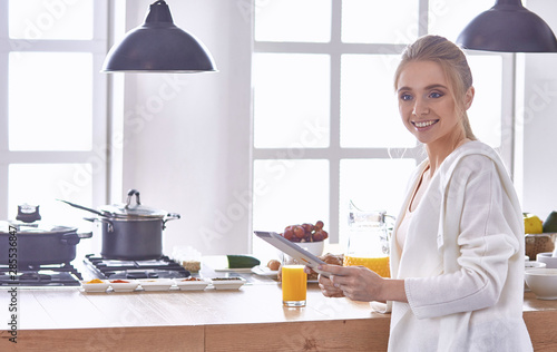 Fototapeta Naklejka Na Ścianę i Meble -  beautiful young woman using a digital tablet in the kitchen