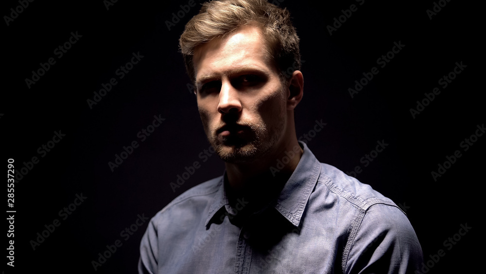 Light illuminating young man on dark background, suspected crime, interrogation