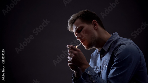 Konstfotografi Young man lighting cigarette in dark room, unhealthy habit, harmful effect