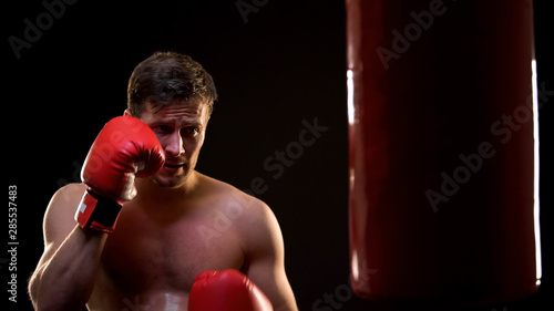Sweaty sportsman training with boxing bag, fighting with insecurities concept